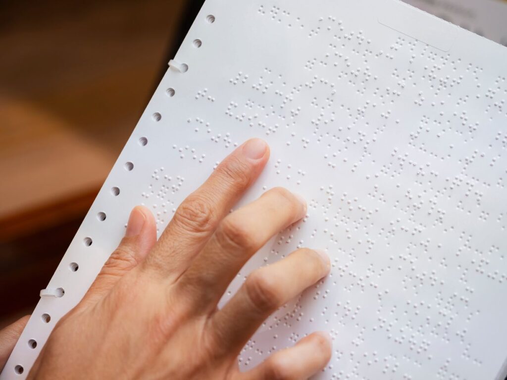 dłoń osoby czytającej tekst pisany Braille'm